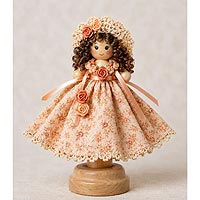 Handmade doll pin mother wearing a floral dress with lace trim, peach ribbon roses, curly brown hair, a crocheted hat, and standing on a wooden doll pin stand.
