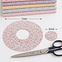 Fabric preparation for a doll pin dress showing a 7-inch fabric circle, 2-inch center cutout, removed center piece, and sewing scissors.