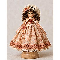 Handmade wooden doll pin doll wearing a peach floral fabric dress with lace trim, ribbon accents, and a crocheted bonnet adorned with miniature roses and curly brown hair, displayed on a wooden doll stand.