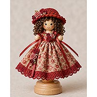 Handmade doll pin doll featuring a red floral dress, crocheted hat with ribbon rose accents, curly brown hair, and a wooden display stand for doll making and decorative crafts.